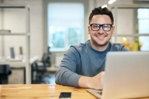 In this Image a Man with a smiling face sitting infron of laptop with his phone looking for his carrer opportunities. Career opportunities in digital marketing, Digital marketing manager jobs, Digital marketing courses with job guarantee, Digital marketing specialist jobs, Digital marketing analyst jobs, Digital marketing job roles